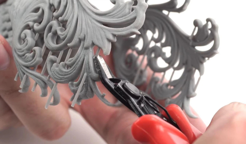 Removing supports from a 3D printed model using flush cutters and needle-nose pliers with gentle twisting motions to avoid damaging the surface