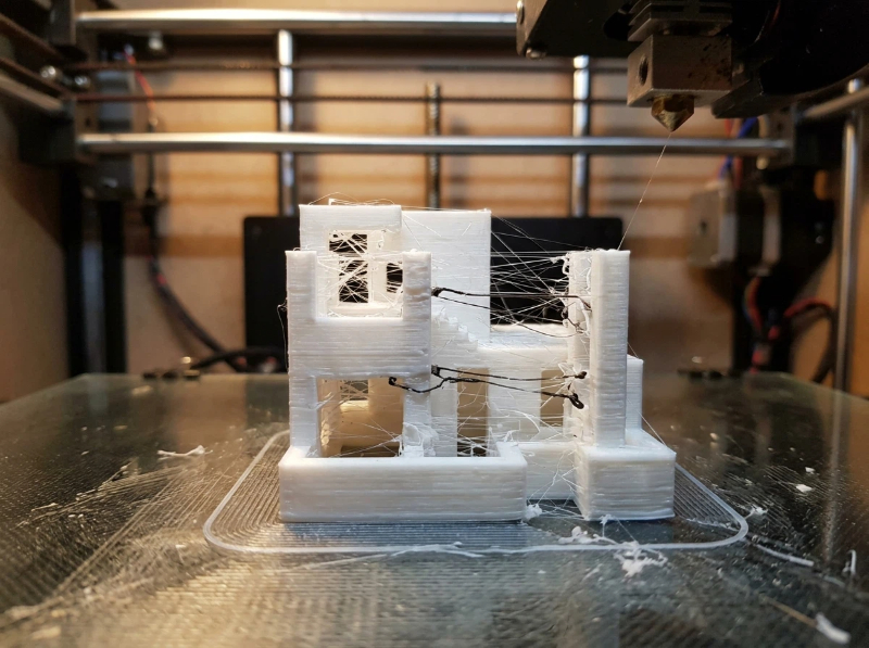 3D print stringing defect showing thin plastic strands between two printed towers caused by insufficient retraction or excessive nozzle temperature